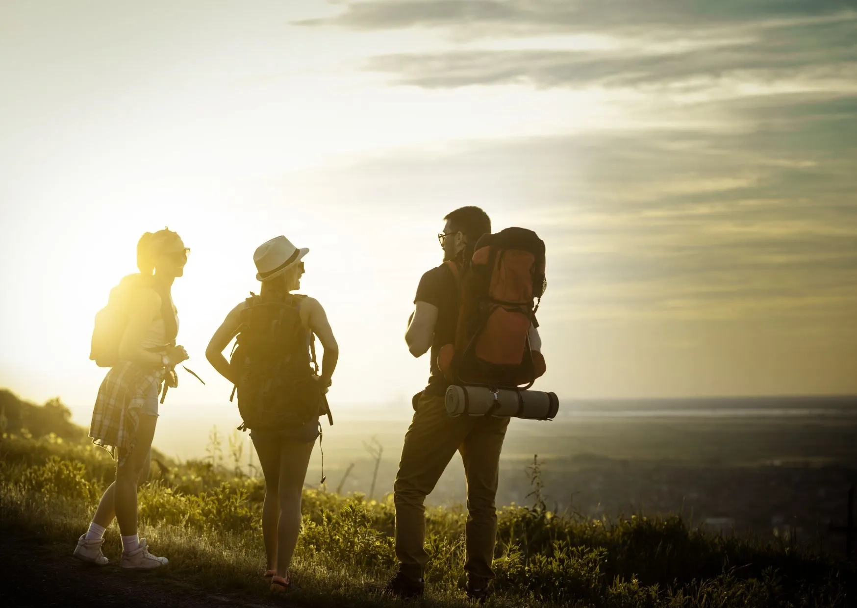 Trois randonneurs avec sacs à dos contemplant le coucher du soleil en montagne.