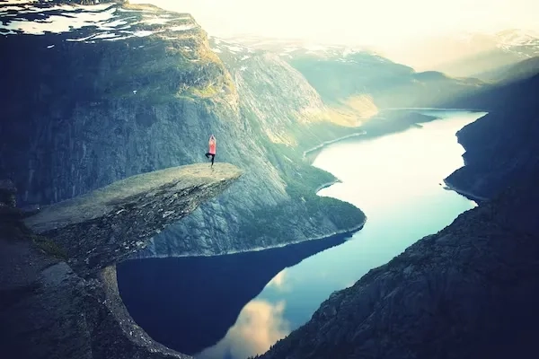 Personne en posture d'équilibre sur un surplomb rocheux étroit, seule face à un paysage de fjord