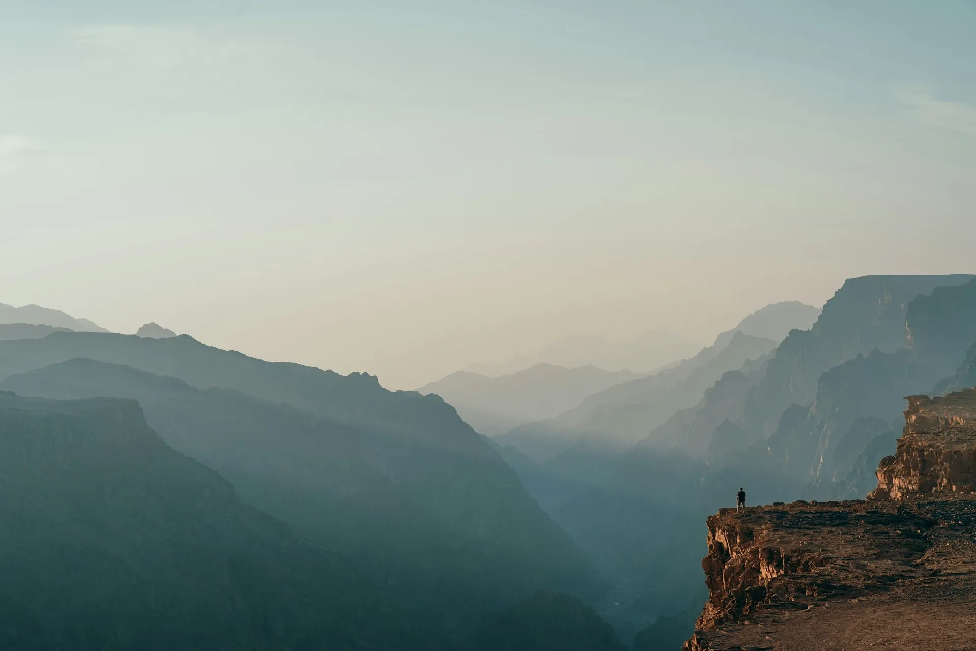 Personne seule au sommet d'une falaise, surplombant des montagnes dans la brume au lever du soleil